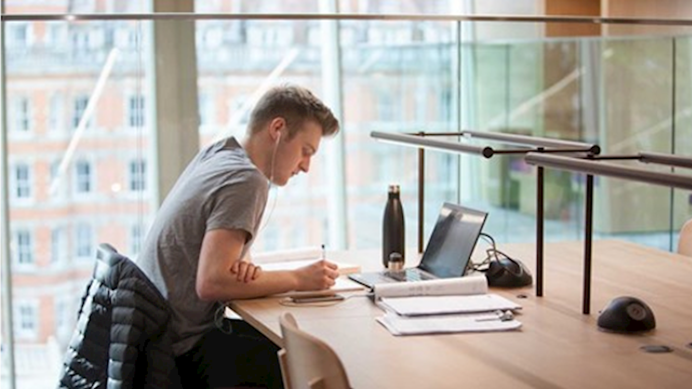 Student in Library with Laptop - Economics