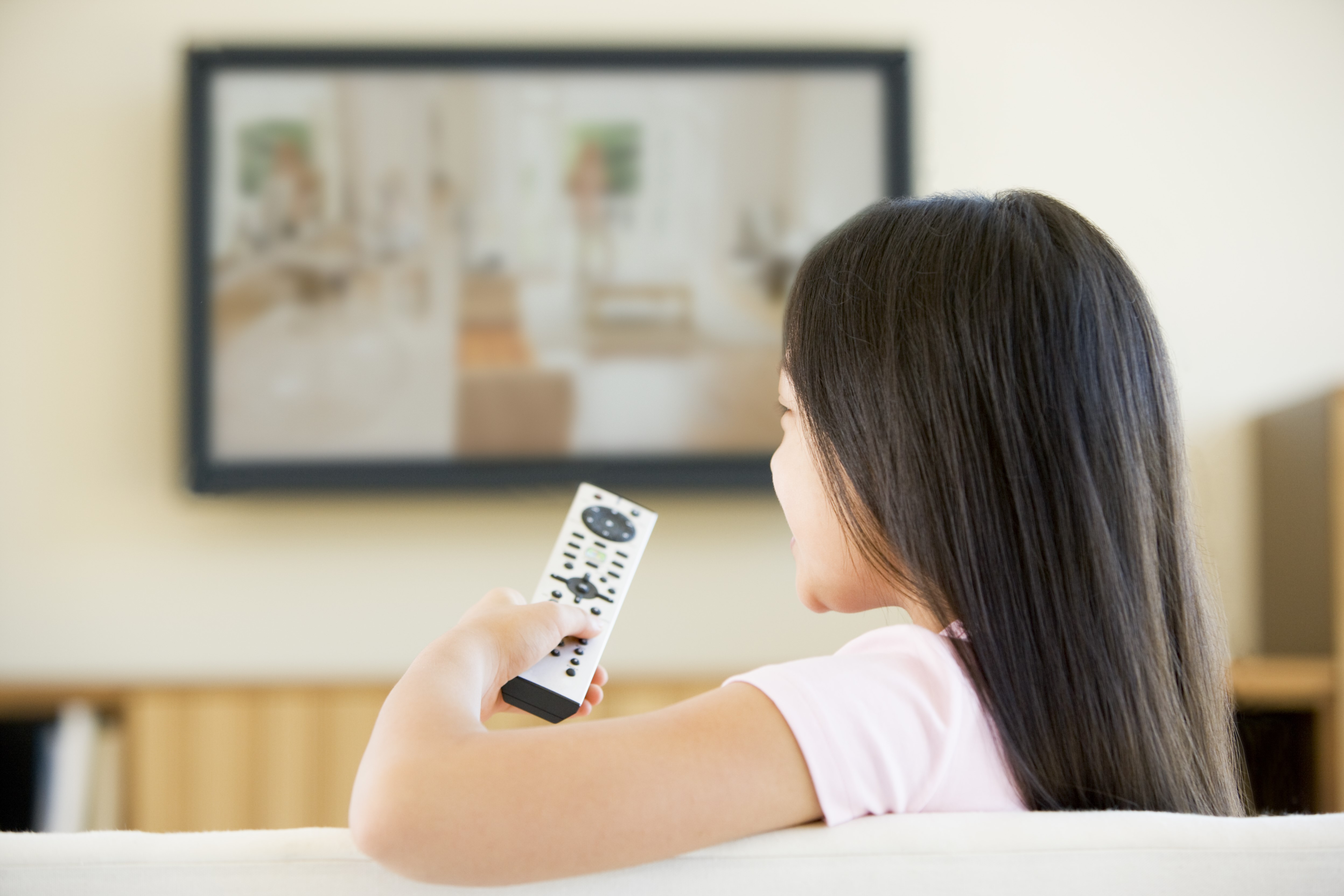 Young female child watching TV with the remote in her hand